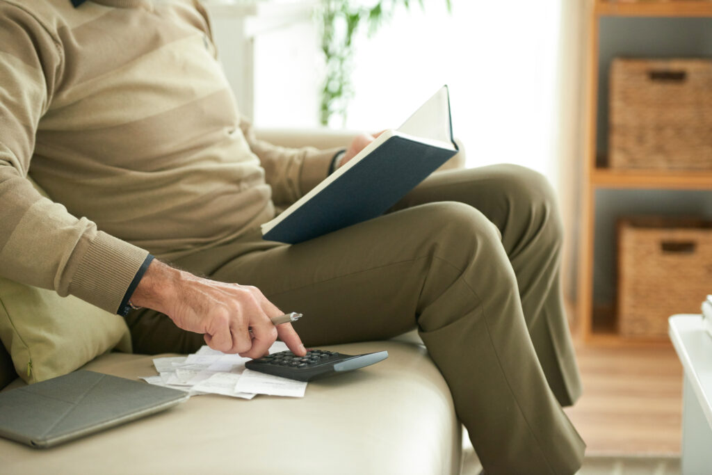 Personne assise sur un canapé calculant ses remboursements de prêt avec une calculatrice