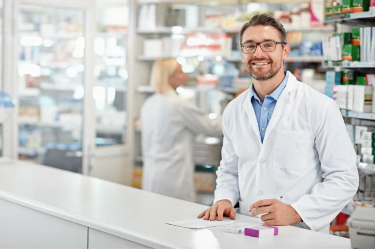 Pharmacien souriant en blouse blanche au comptoir de son officine