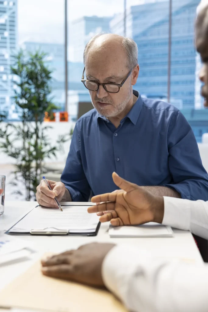 Un courtier accompagne un client senior dans la signature de son contrat d’épargne