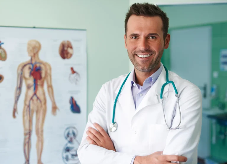 Médecin souriant, bras croisés, devant une planche anatomique